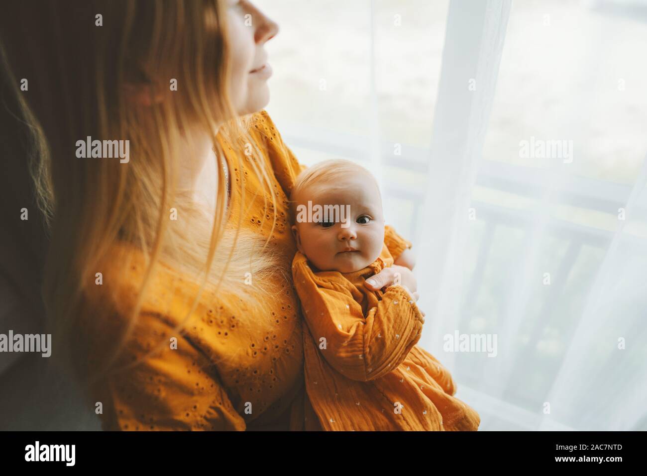 Fille mère avec bébé bébé vie familial maman et enfant ensemble à la maison de vacances fête des Mères la maternité concept robe couleur moutarde Banque D'Images