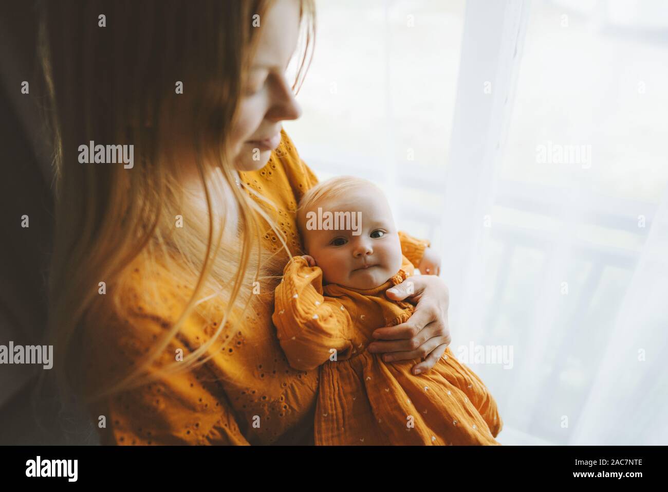 Mother holding baby fille vie familial maman et bébé ensemble à la maison de vacances de jour de mères concept maternité couleur moutarde dress Banque D'Images