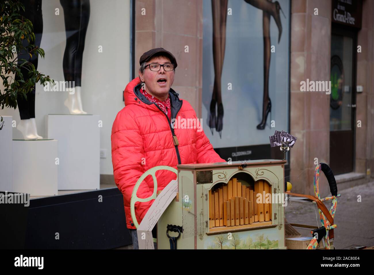 Orgue de Barbarie en tournant le volant de son instrument, vêtu de vêtements d'hiver, dans les rues de Strasbourg, France. Banque D'Images