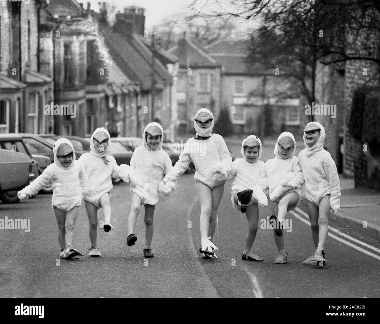 Années 1980, historiques, 'Duck derby", les jeunes enfants dans une rue urbaine tenant la main et portant des costumes de canard, composé d'un costume de canard, canard en forme de tête du capot et surchaussures, England, UK. Banque D'Images