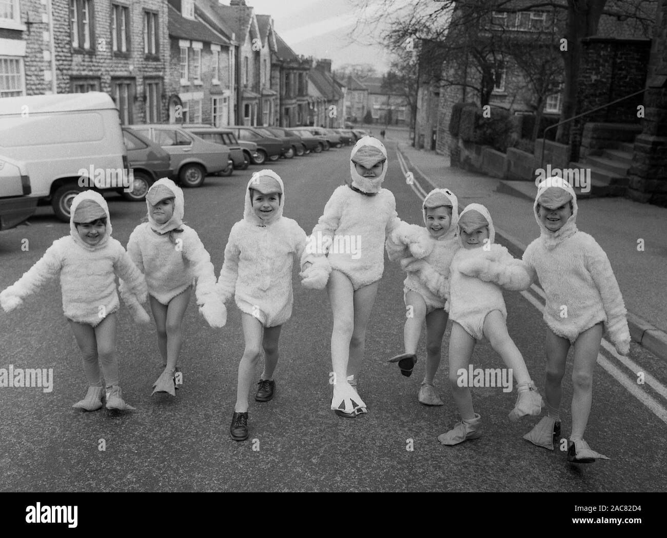 Années 1980, historiques, 'Duck derby", les jeunes enfants dans une rue urbaine tenant la main et portant des costumes de canard, composé d'un costume de canard, canard en forme de tête du capot et surchaussures, England, UK. Banque D'Images