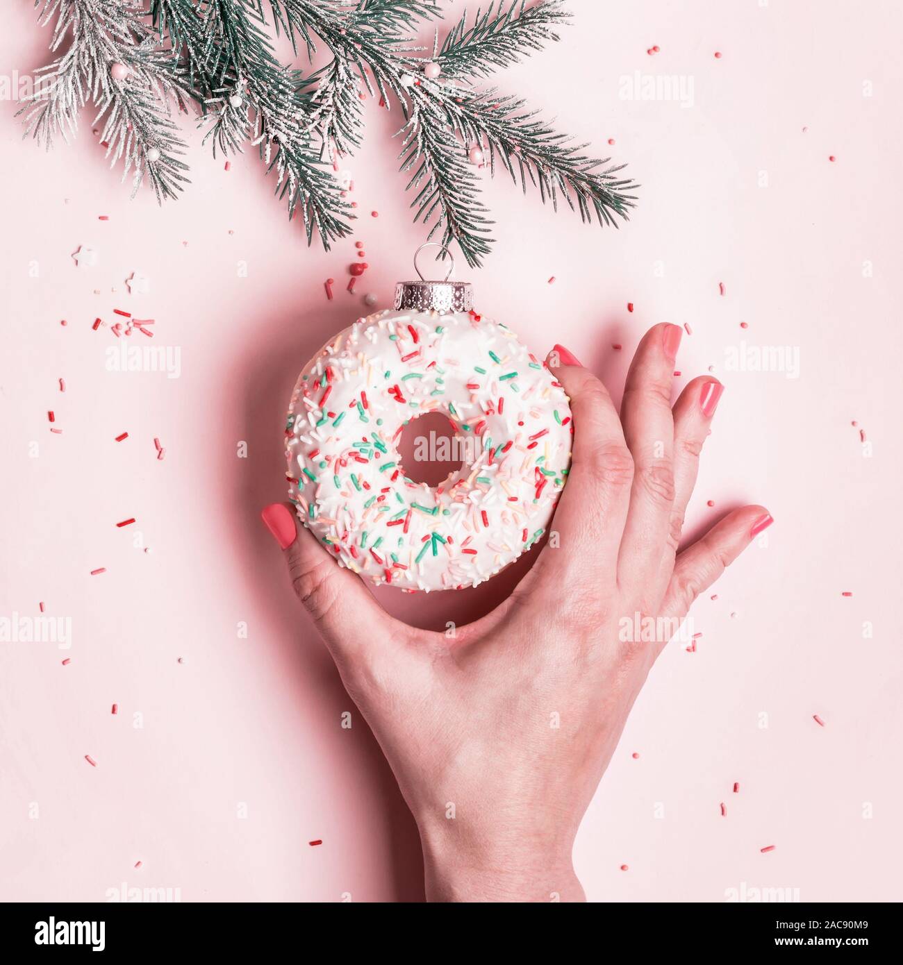 Main femme raccroche Boule de Noël faite de beigne glacé sur fond rose. Concept créatif de Noël. Banque D'Images