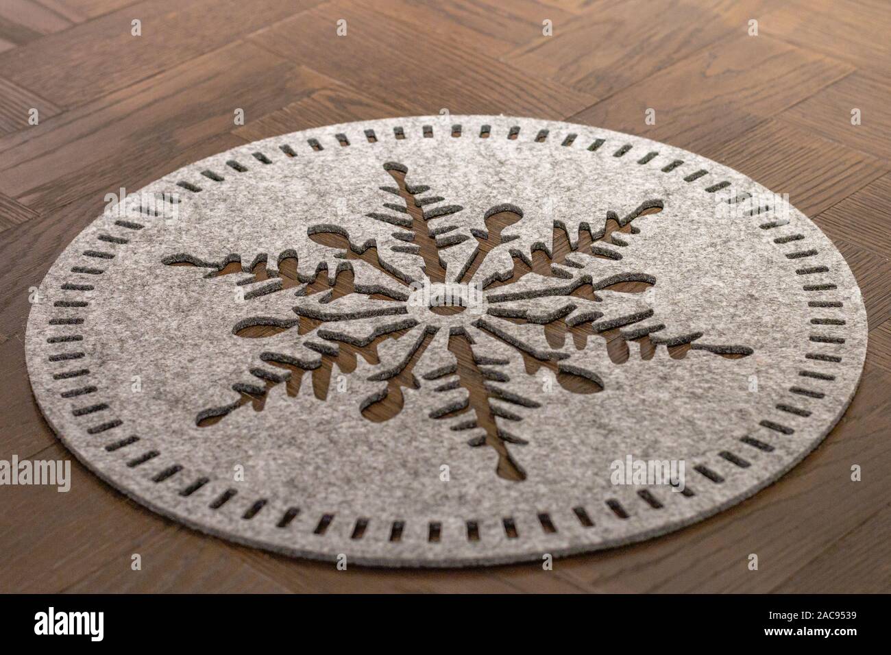 Un feutre de laine gris clair mat plat rond en forme de flocon de neige est posé sur une table en bois foncé Banque D'Images