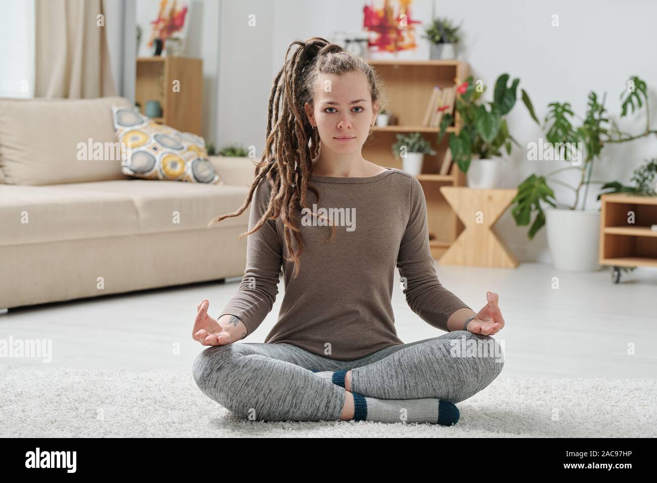 Serene girl à activewear traversant les jambes tout en pratiquant le yoga sur le plancher Banque D'Images