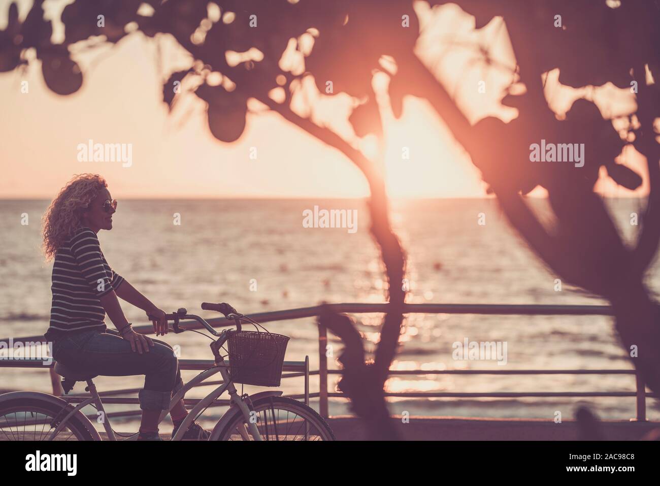 Belle femme de race blanche adultes avec des cheveux blonds pour le coucher du soleil avec vue sur la mer de l'océan sur un vélo à la mode vintage - activité de loisirs et de plein air Banque D'Images