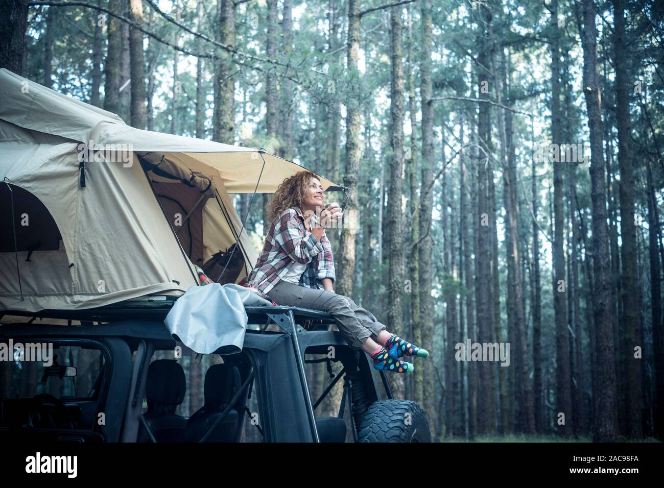 Heureux de belles personnes caucasian woman s'asseoir sur le toit de la voiture avec tente montée sur elle pour travel camping lifestyle - wanderlust veh Banque D'Images