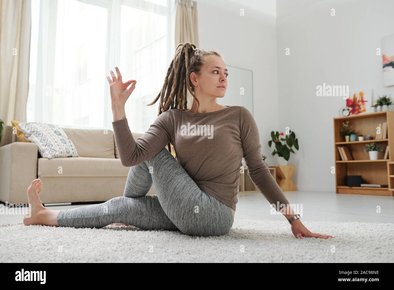 Jeune femme avec des dreadlocks assis sur le plancher d'une des positions de yoga Banque D'Images