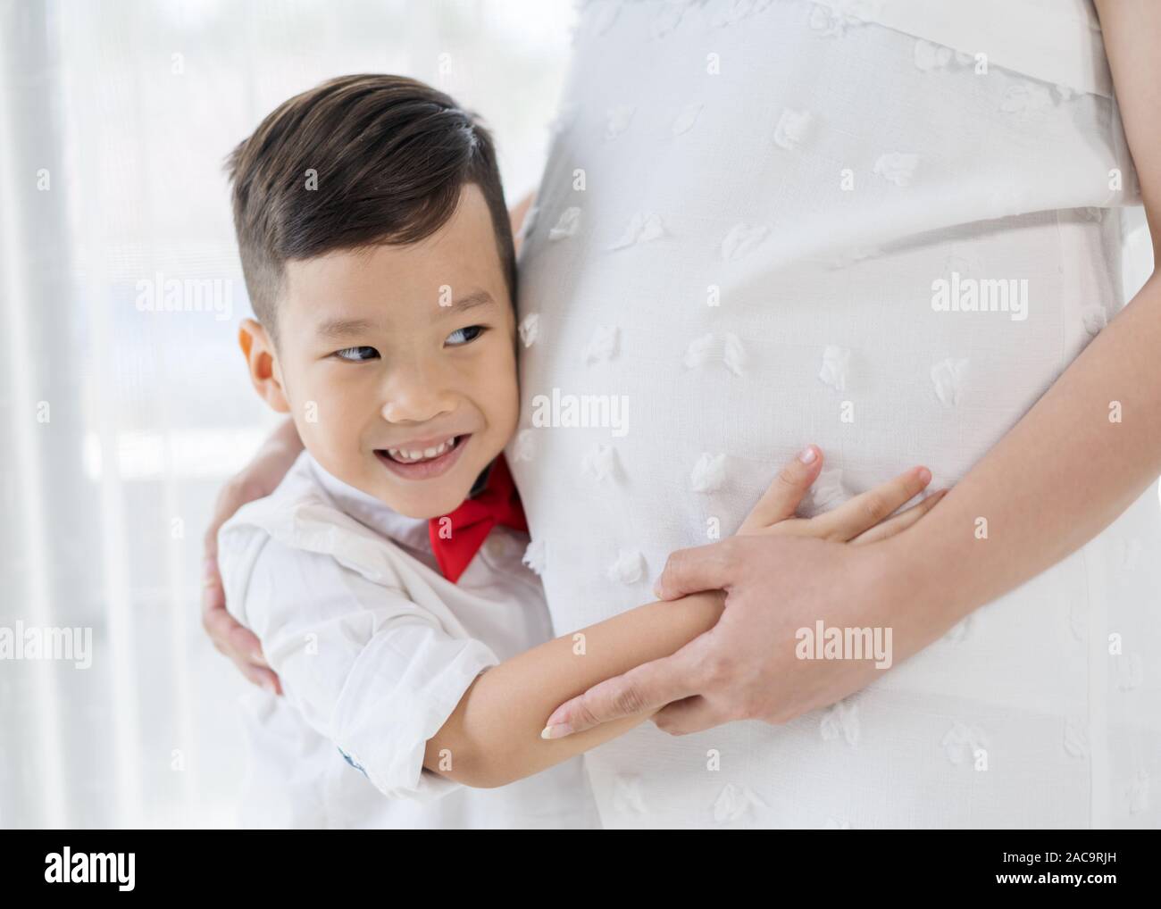 Happy child boy hugging et écoute le ventre de sa mère enceinte Banque D'Images