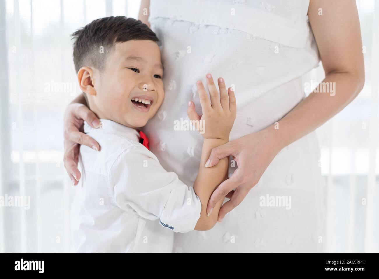 Happy child boy hugging et écoute le ventre de sa mère enceinte Banque D'Images