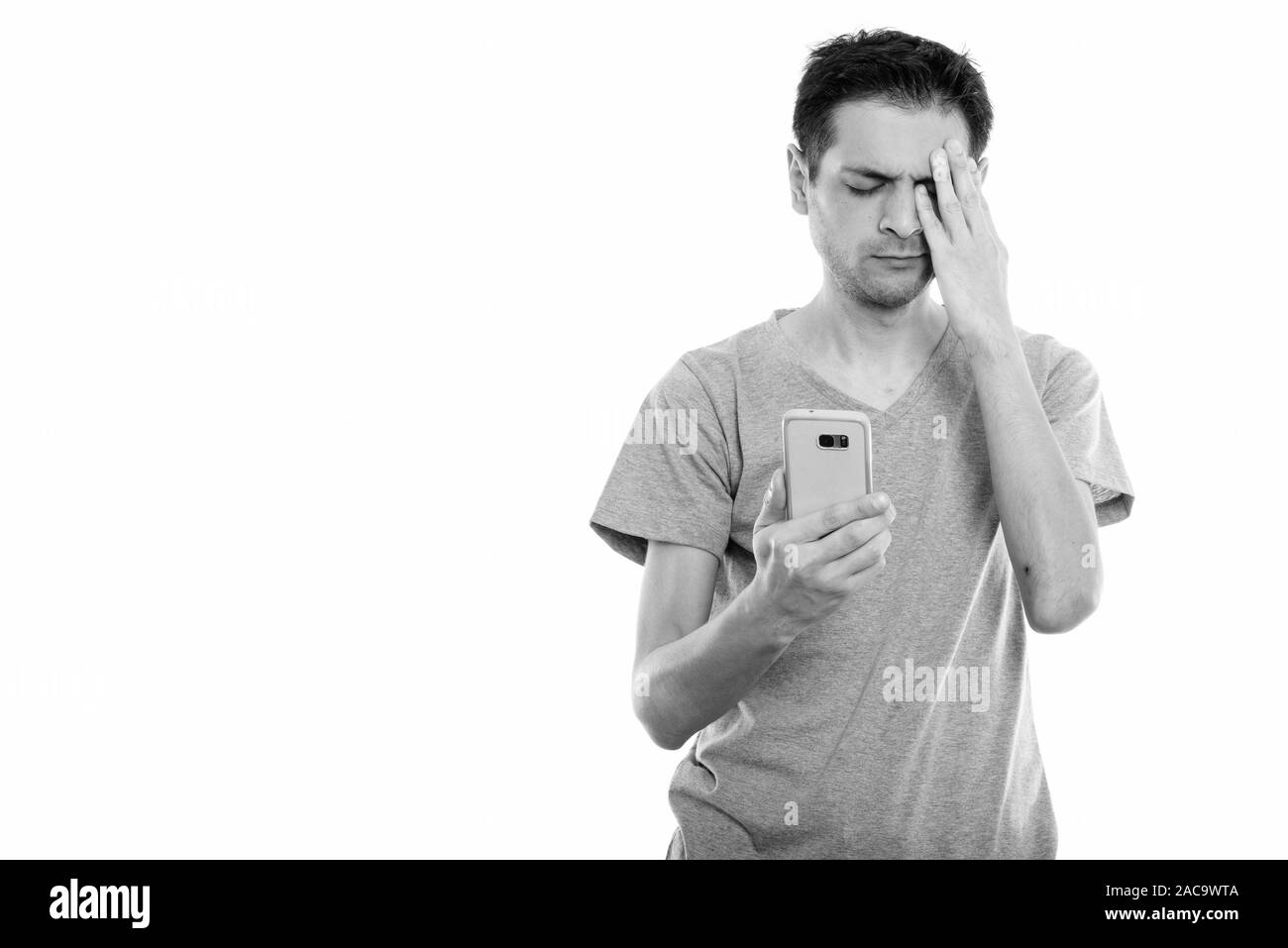 Studio shot of young man using mobile phone while looking a souligné Banque D'Images