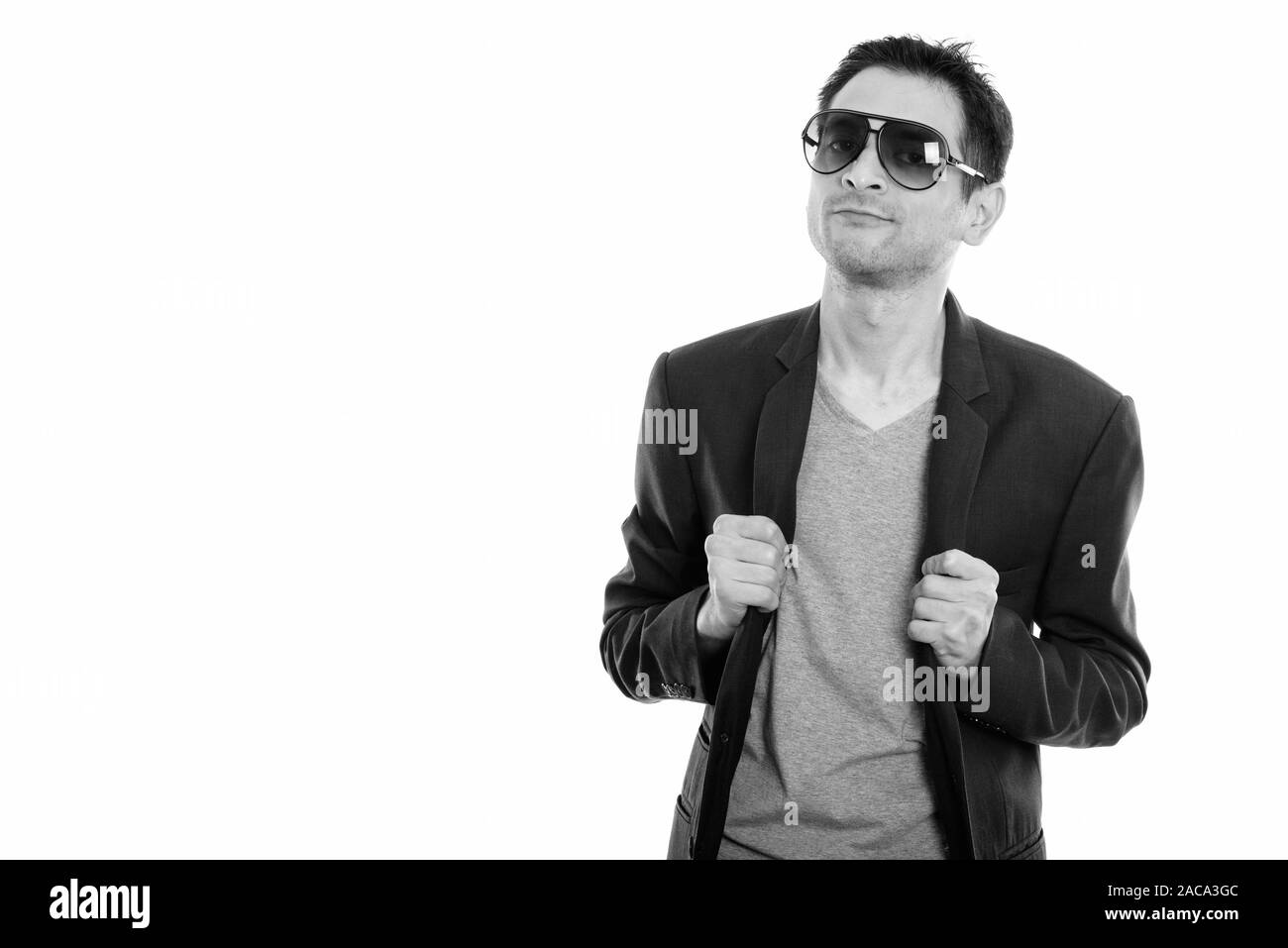 Studio shot of cool heureux jeune homme souriant et portant des lunettes de soleil tout en fixant sa veste Banque D'Images