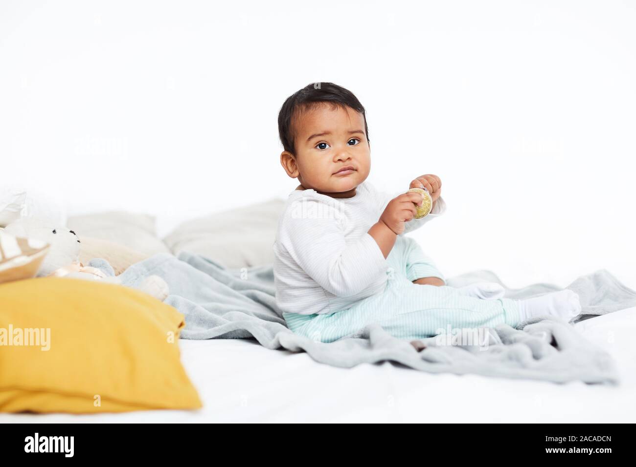 Cute baby girl africaine assise sur le lit et de jouer avec des jouets Banque D'Images