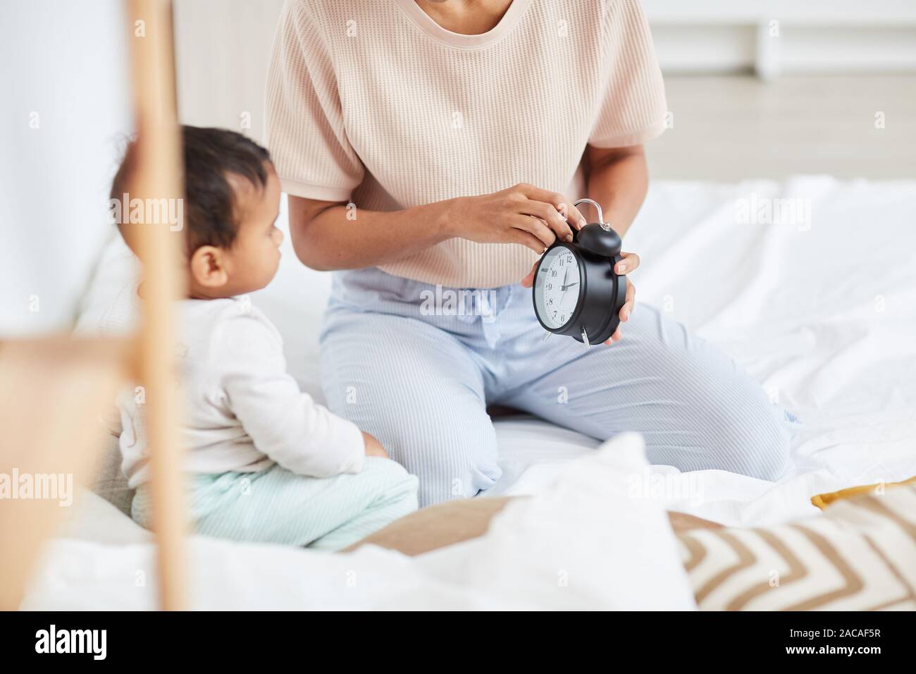 Close-up of mother holding réveil et contrôler le temps avec bébé assis sur le lit et en regardant réveil Banque D'Images