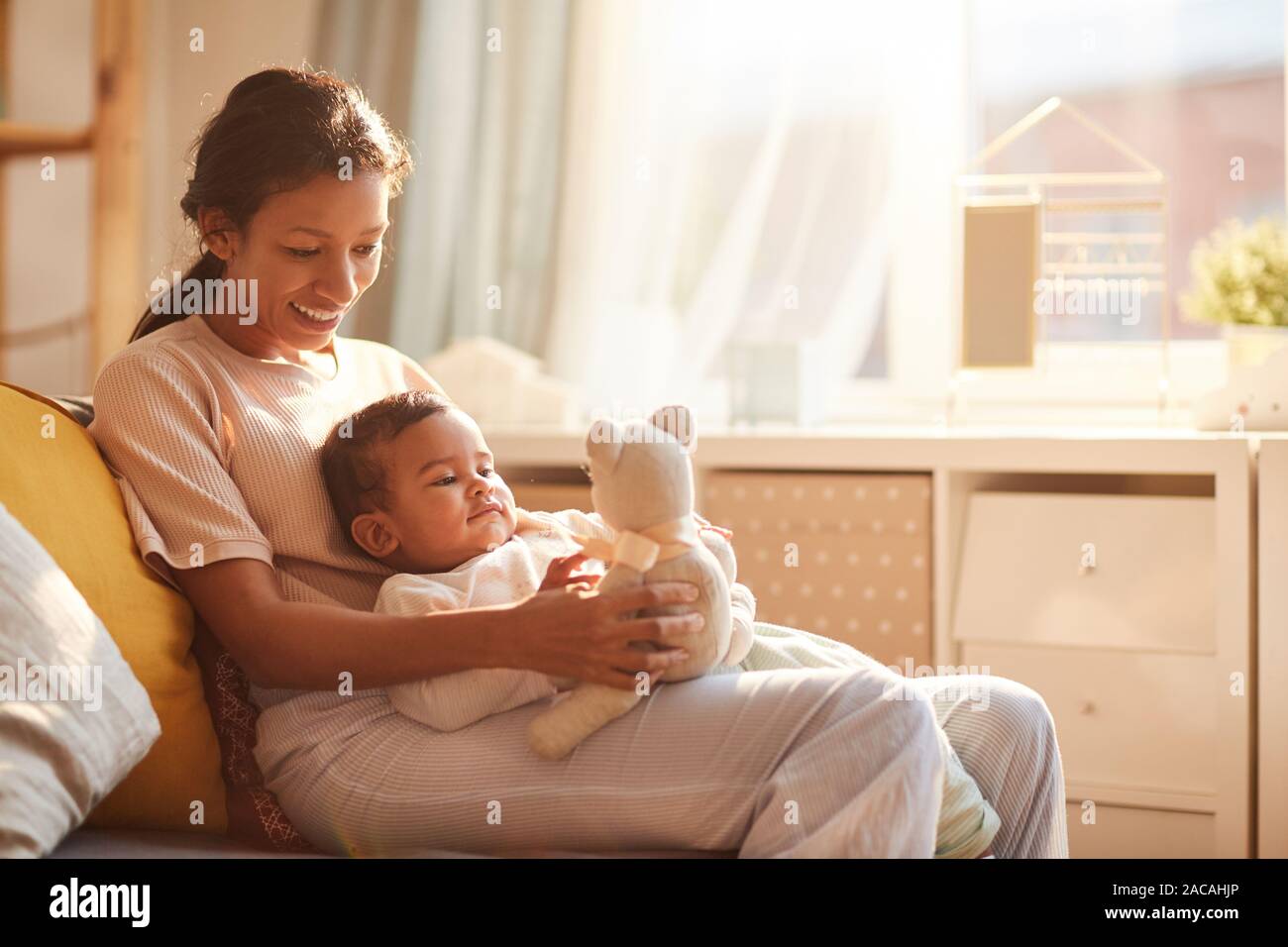 Heureux jeune mère avec bébé sur ses genoux Playing with toy à la maison Banque D'Images
