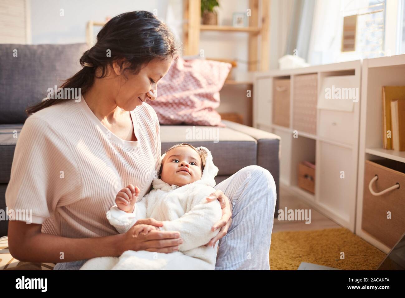Jeune mère tenant son bébé sur les mains et le berçant tout en restant assis sur le sol dans la chambre Banque D'Images