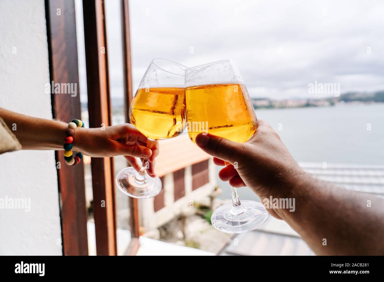 Détail des mains de deux people toasting with beer dans la fenêtre d'un restaurant avec vue sur la mer Banque D'Images