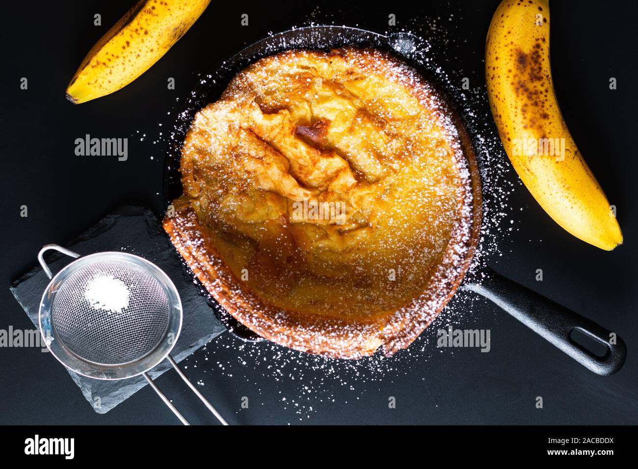 Concept alimentaire néerlandais ou allemand bébé Maison garniture au caramel de bananes dans la poêle à crêpes en fonte de fer sur fond noir Banque D'Images