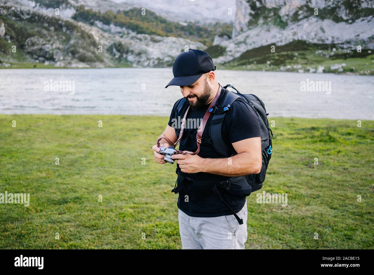 Caucasian man with cap et la barbe fait des photos avec un appareil photo de visites dans un paysage de montagne avec un lac Banque D'Images