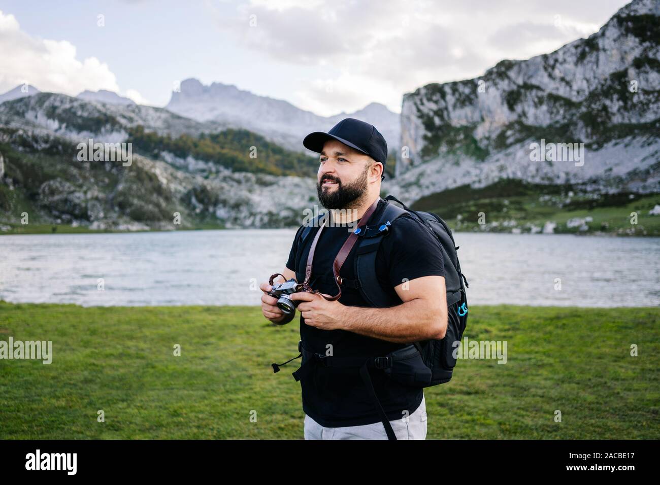 Caucasian man with cap et la barbe fait des photos avec un appareil photo de visites dans un paysage de montagne avec un lac Banque D'Images