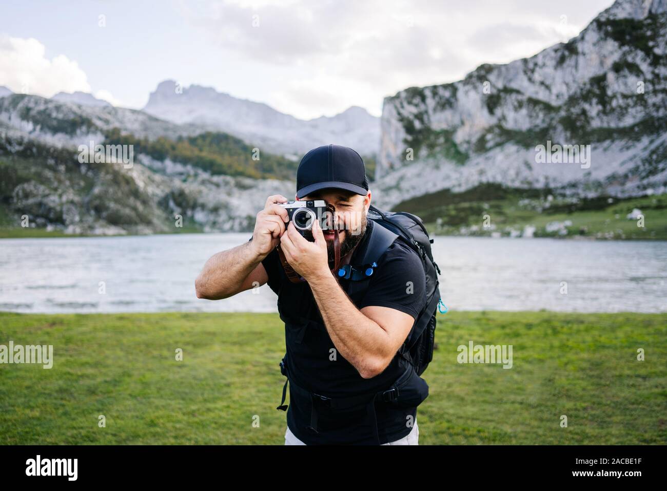 Caucasian man with cap et la barbe fait des photos avec un appareil photo de visites dans un paysage de montagne avec un lac Banque D'Images