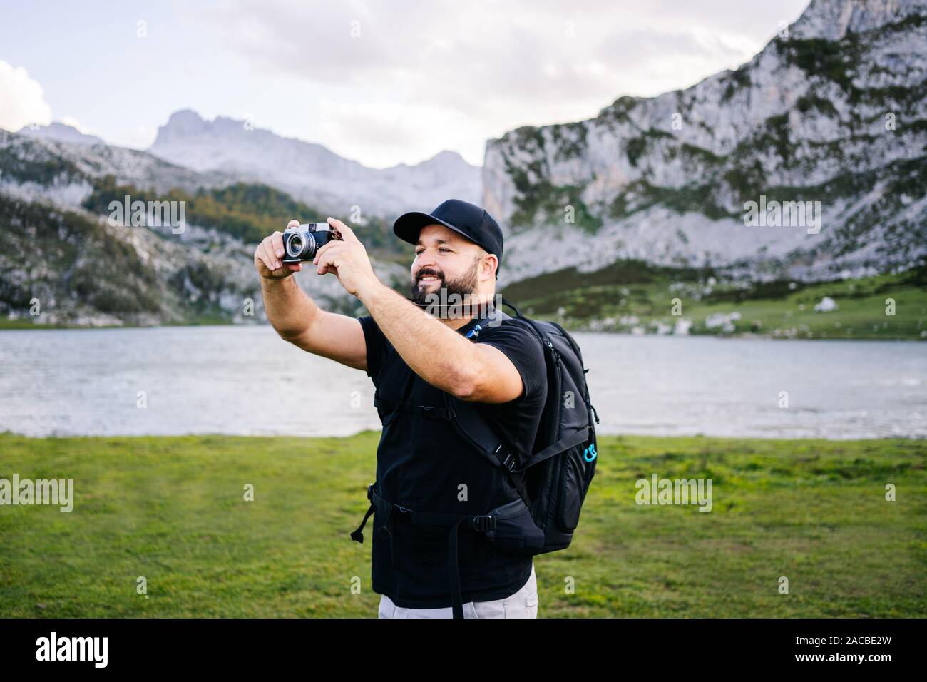 Caucasian man with cap et la barbe fait des photos avec un appareil photo de visites dans un paysage de montagne avec un lac Banque D'Images