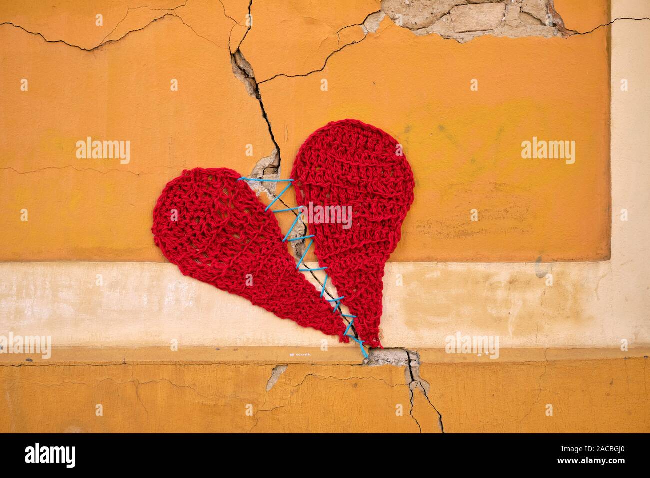 Mur de béton avec une fissure, couvert par un tricot de laine de deux parties de cœur maintenu ensemble par une seule chaîne. Banque D'Images