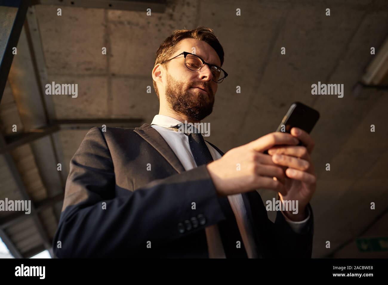 Low angle view of bearded man in suit l'article en ligne et de travail à l'aide de son téléphone portable Banque D'Images