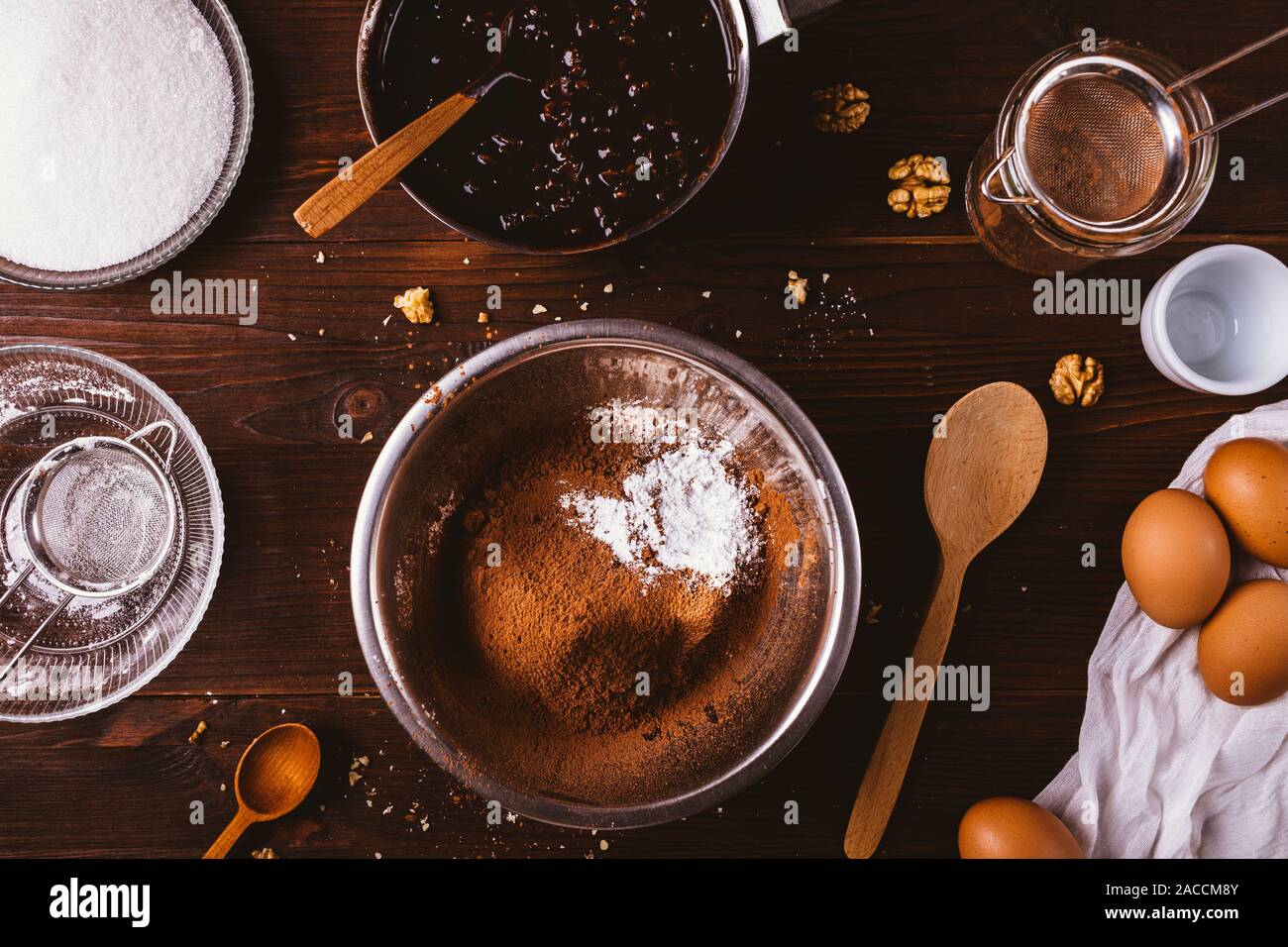 Bol en métal avec du cacao en poudre et la farine tamisée à côté de chocolat fondu, les noix et les œufs ingrédients pour de délicieux gâteaux faits maison sur brownie woode Banque D'Images
