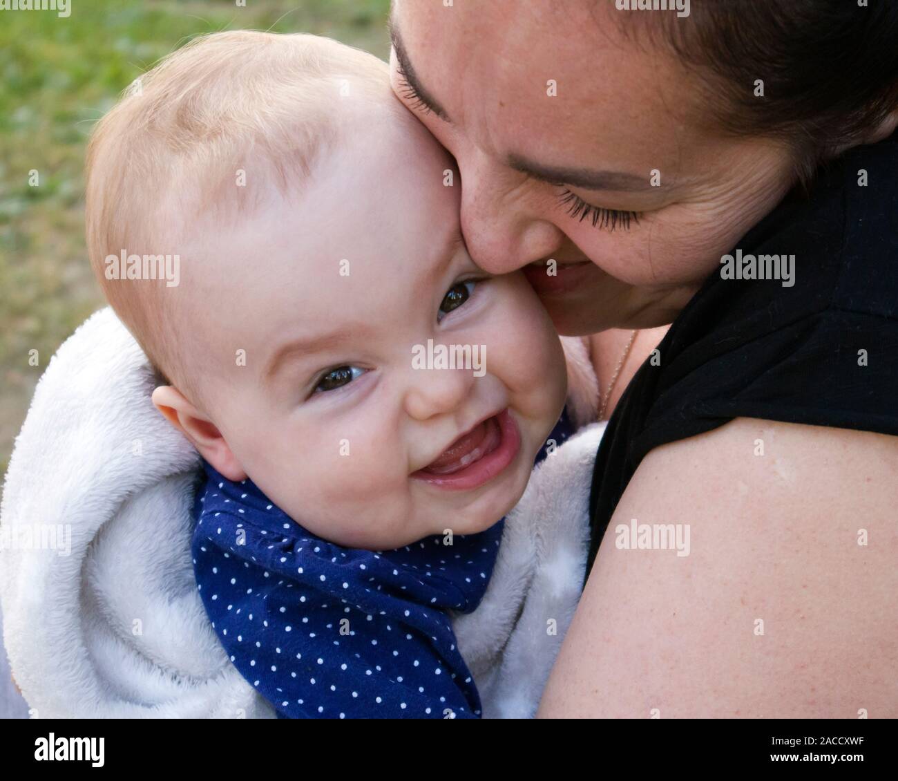Adorable bébé fille souriante dans les bras de sa mère heureuse Banque D'Images