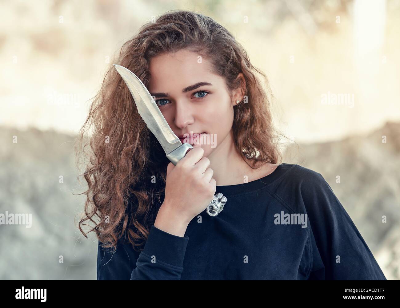Cheveux bouclés. Belle fille avec les cheveux ondulés avec grand couteau, une lame près de la face, menace. Banque D'Images