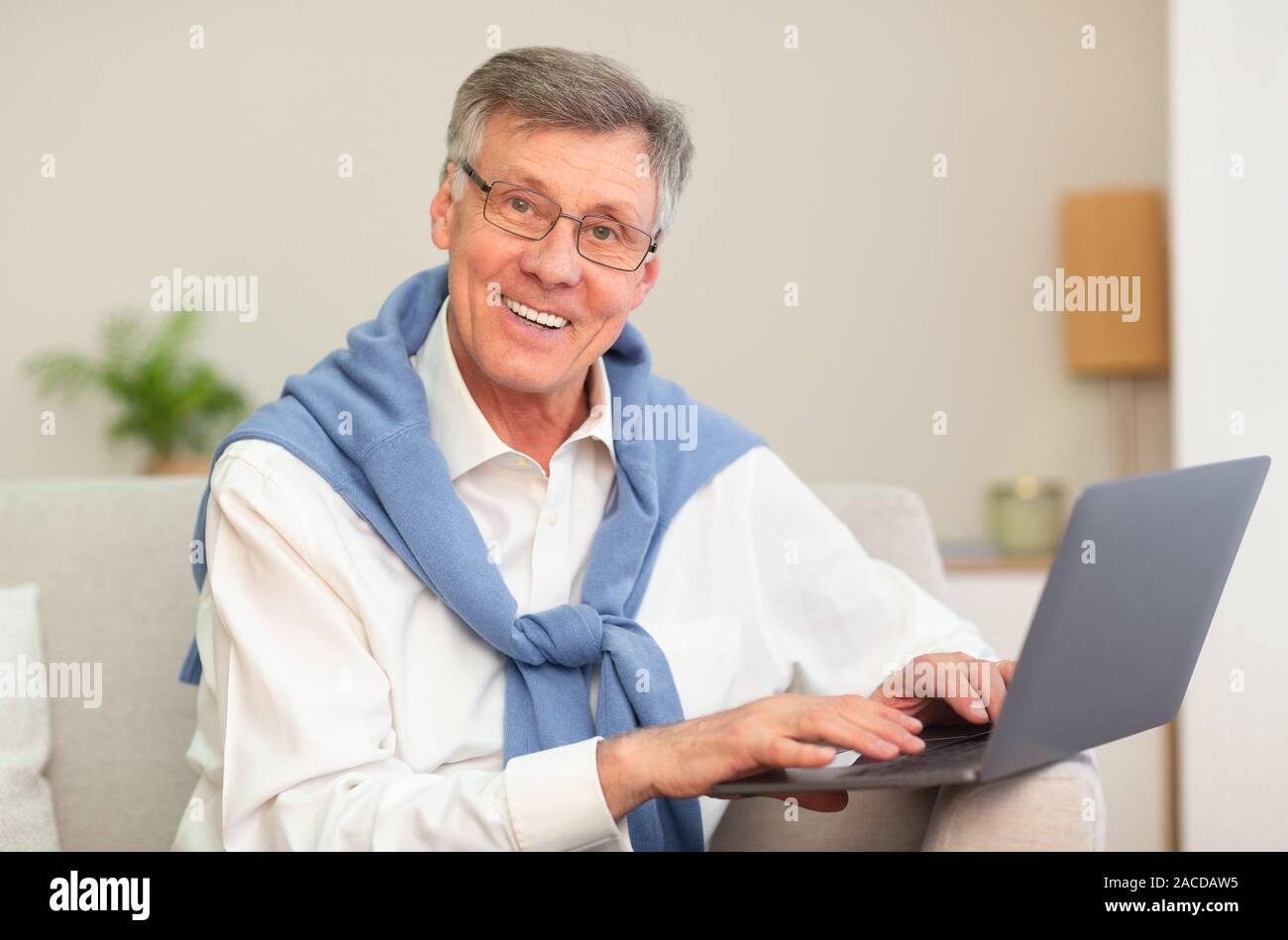 Ordinateur portable à l'aide d'homme Senior Smiling Sitting on Sofa Indoor Banque D'Images