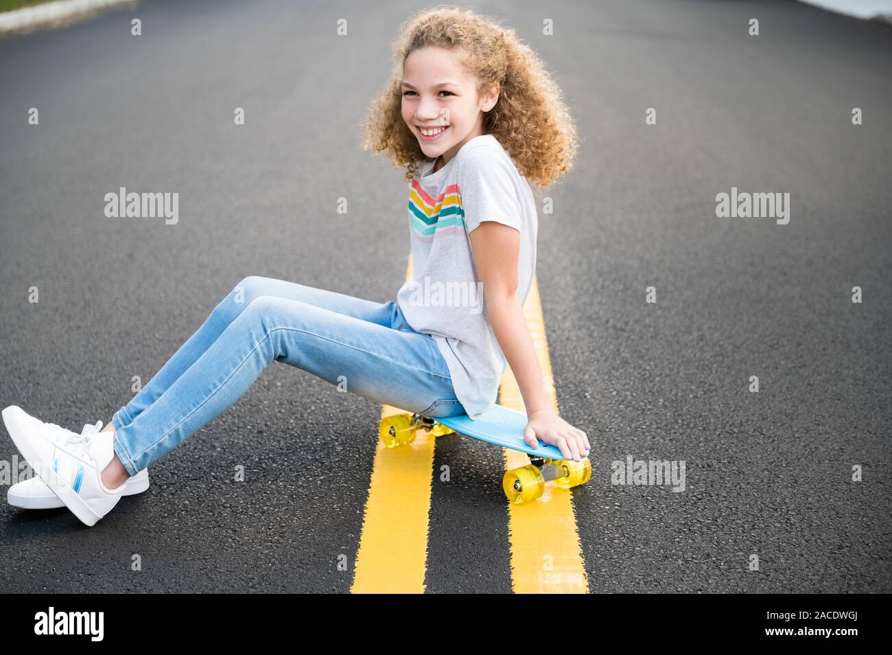 Fille assise sur un skateboard sur la route Banque D'Images
