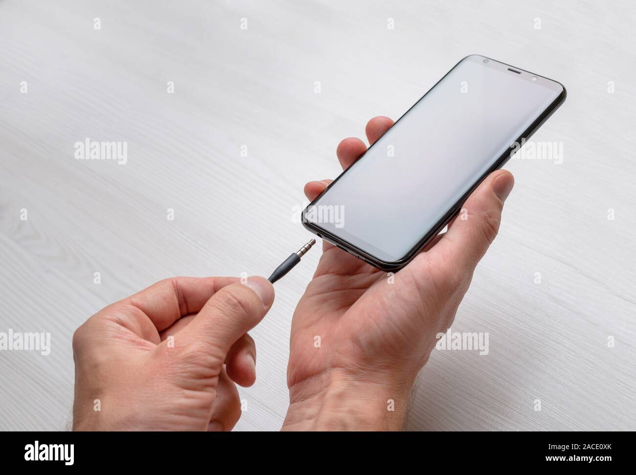 La connexion de la prise audio sur un téléphone mobile. Prise audio 3,5 mm et d'un téléphone mobile dans les mains. Banque D'Images