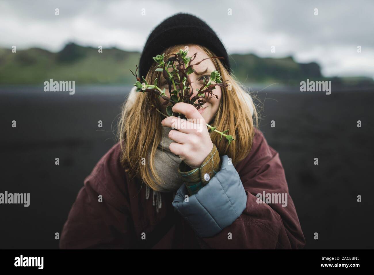 Femme tenant des plantes sur son visage sur la plage Banque D'Images