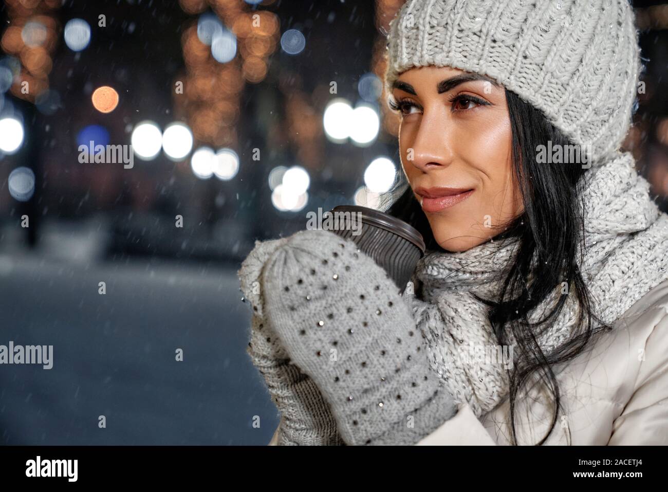 Belle fille de bonnet, écharpe en tricot de laine et des gants holding  Coffee cup en hiver. Fille charmante en vêtements élégants sur fond de nuit  ville avec Photo Stock - Alamy