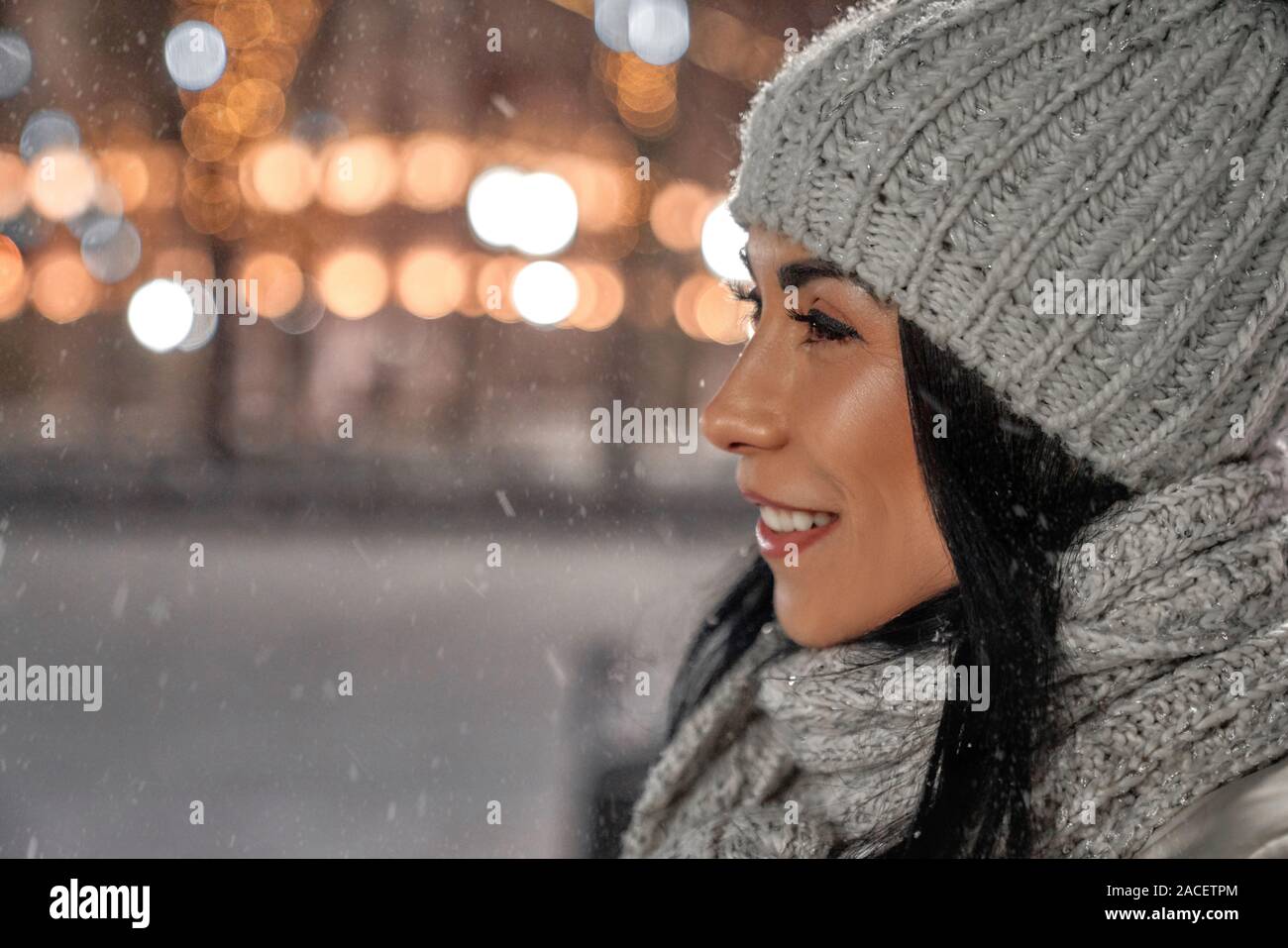 Modèle positif dans l'élégant tricoté en laine bonnet et écharpe sur fond  de nuit rue de noël. Belle Dame avec une peau parfaite et de longs cheveux  noirs smi Photo Stock -