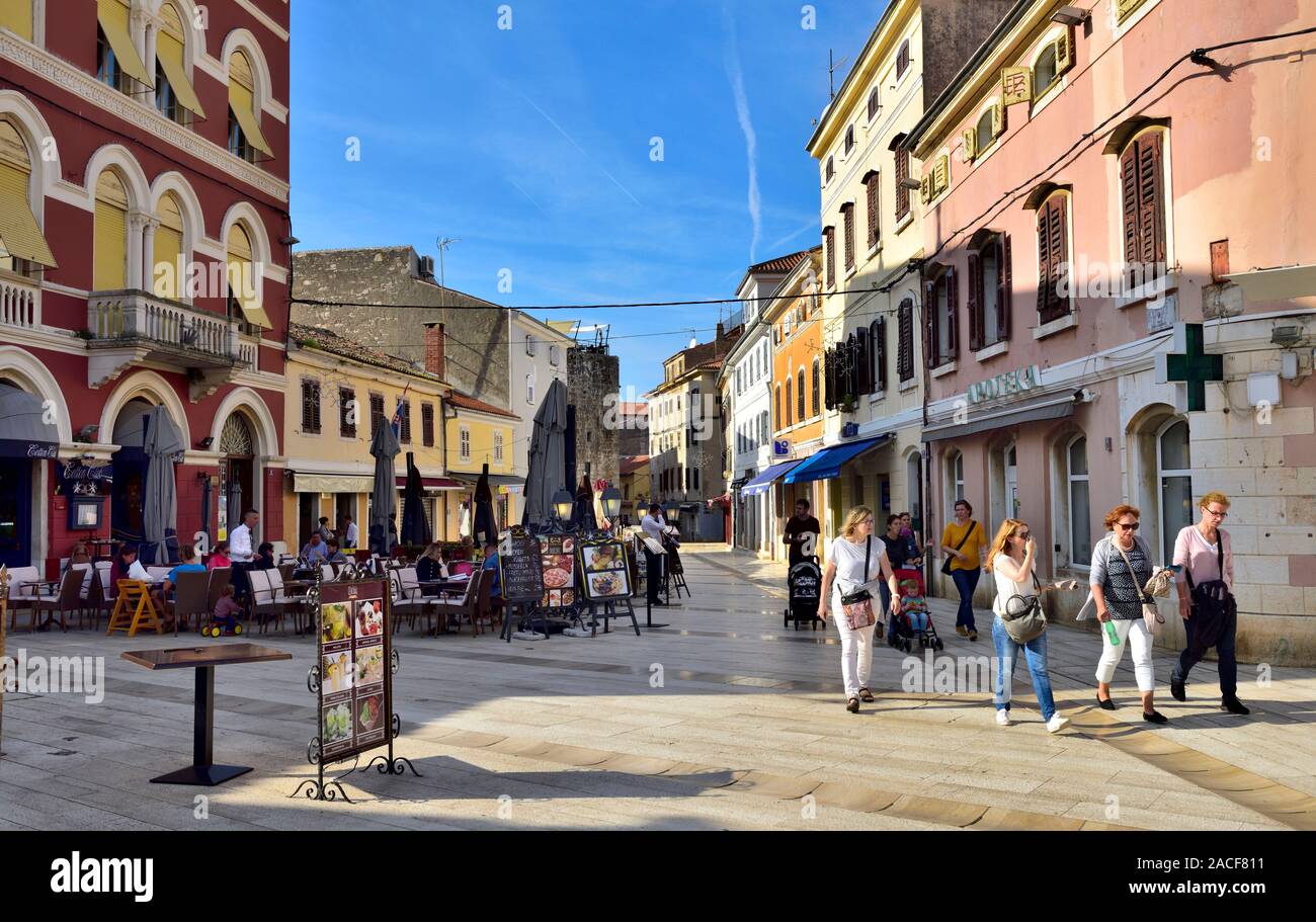 Diners manger dehors au Cotton Club restaurant à main square, Place de la Liberté (Trg Slobode) avec les touristes et les familles en passant devant, Porec, Croatie Banque D'Images