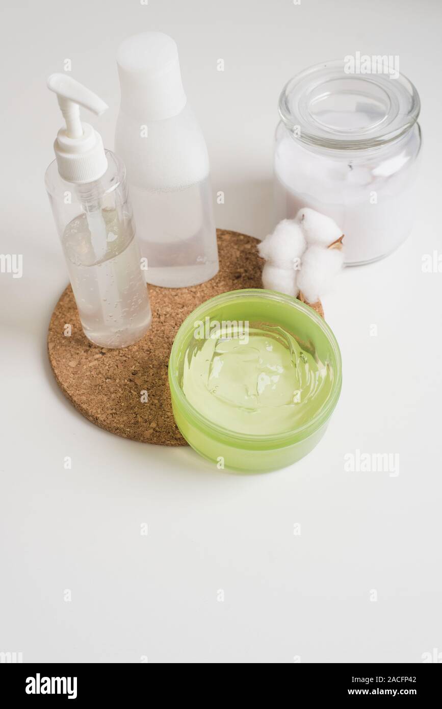 Accueil Soins de la peau, l'eau micellaire, crème et une bougie avec un coton fleur sur la table de chevet. Corps blanc et les cosmétiques de soins de la peau dans un moderne blanc ba Banque D'Images