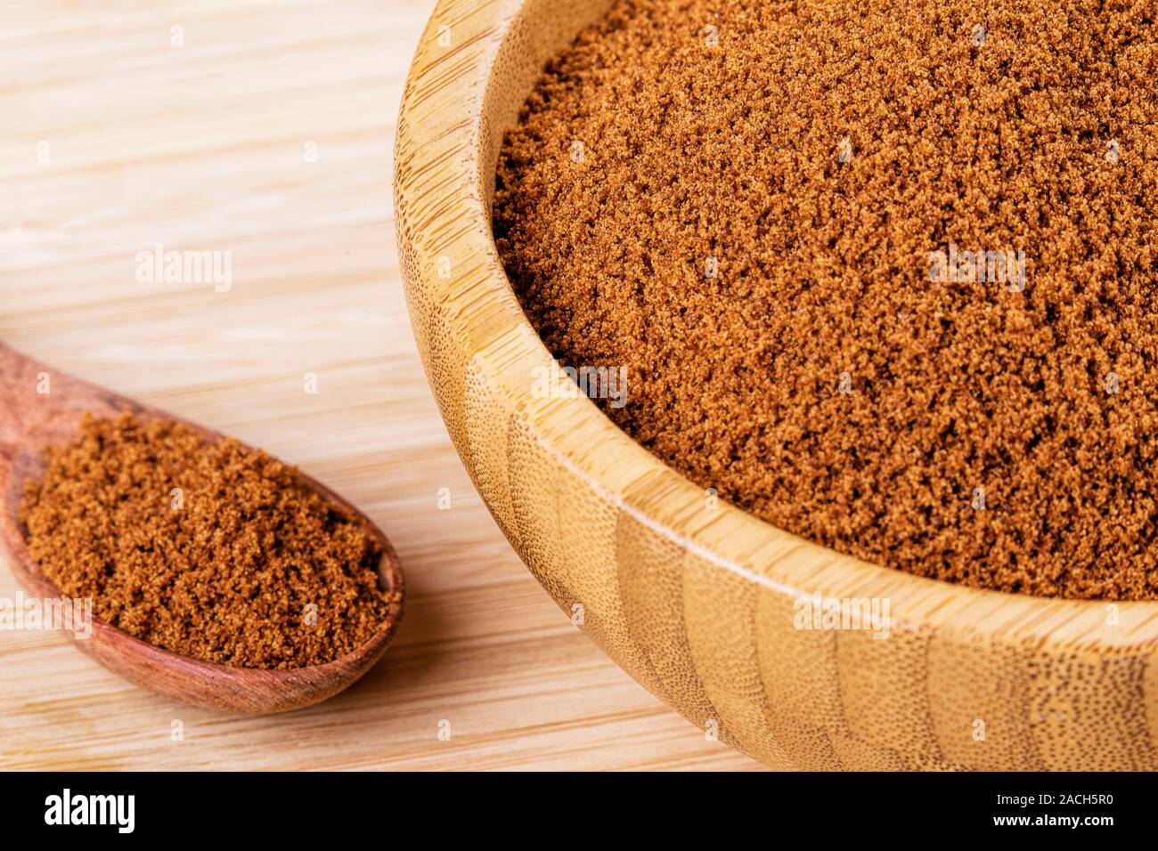 Bol en bois plein de sucre brun foncé avec une cuillère en bois sur un fond de bois Banque D'Images