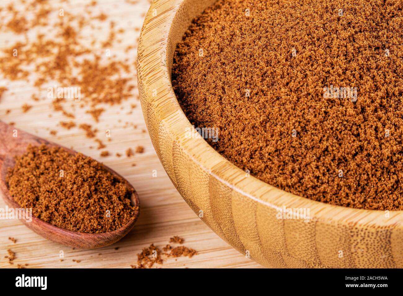 Bol en bois plein de sucre brun foncé avec une cuillère en bois sur un fond de bois Banque D'Images
