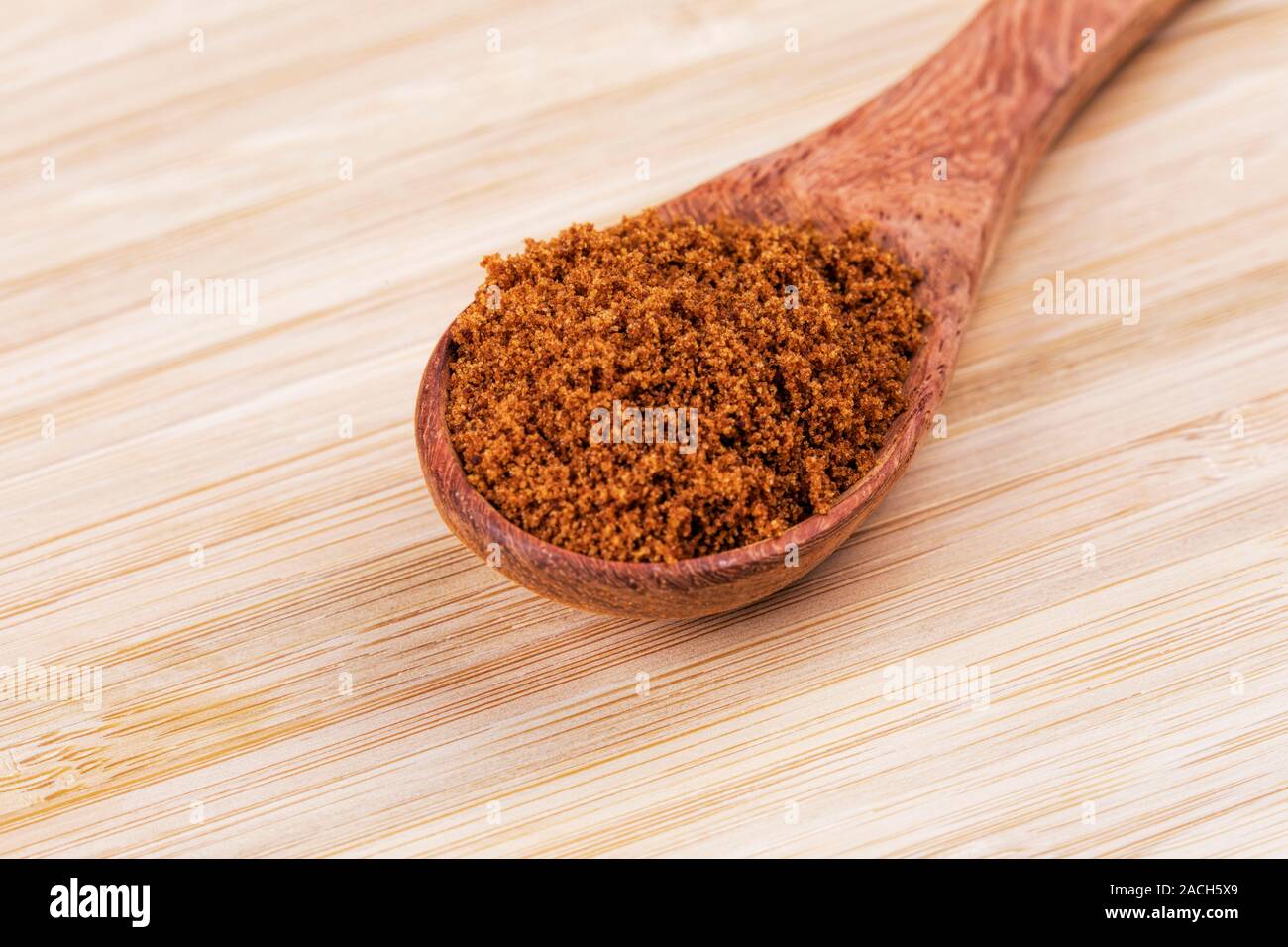 Cuillère en bois plein de sucre brun foncé sur un fond de bois Banque D'Images