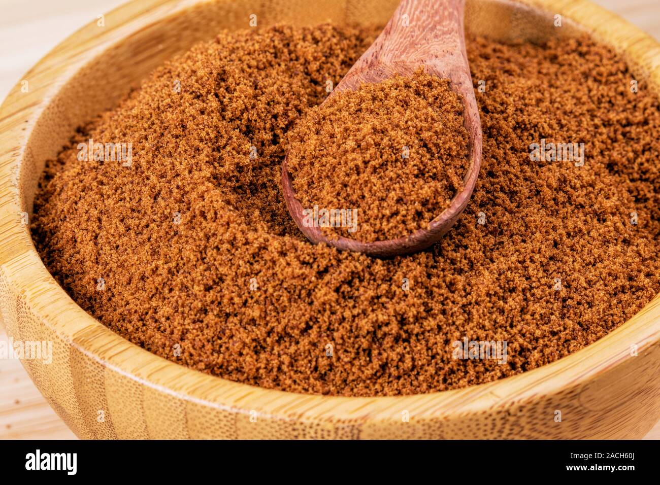 Bol en bois plein de sucre brun foncé avec une cuillère en bois sur un fond de bois Banque D'Images