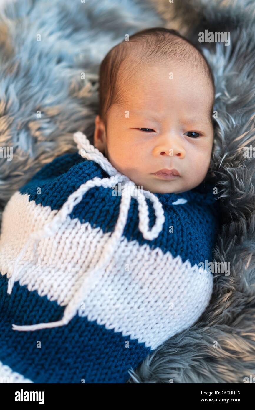 Bébé garçon nouveau-né emmailloté dans une enveloppe en tricot sur un lit  de fourrures Photo Stock - Alamy