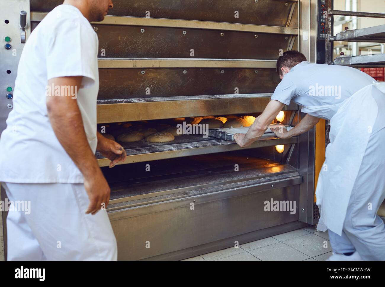 Deux boulangers sont poussant un plateau de pain dans le four à la boulangerie Banque D'Images