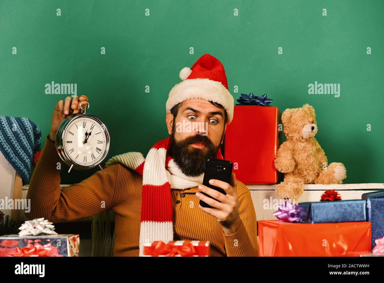 Célébration des gadgets et concept. Homme avec barbe et choqué face vérifie de temps sur téléphone. Santa est titulaire cellulaire et un vieux réveil. Le père Noël fait de vidéo conférence sur téléphone mobile sur fond vert Banque D'Images