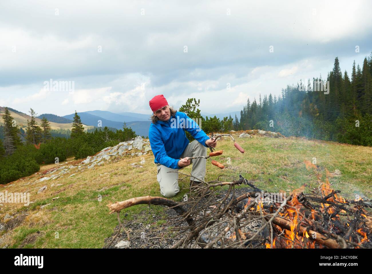 Homme randonnée préparer de délicieuses saucisses sur feu de bois Banque D'Images