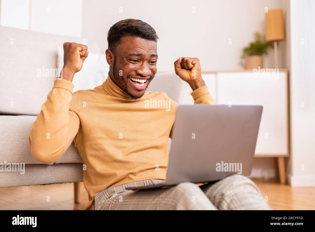 Guy Afro Holding Laptop célébrant la réussite de l'entreprise à la maison Banque D'Images