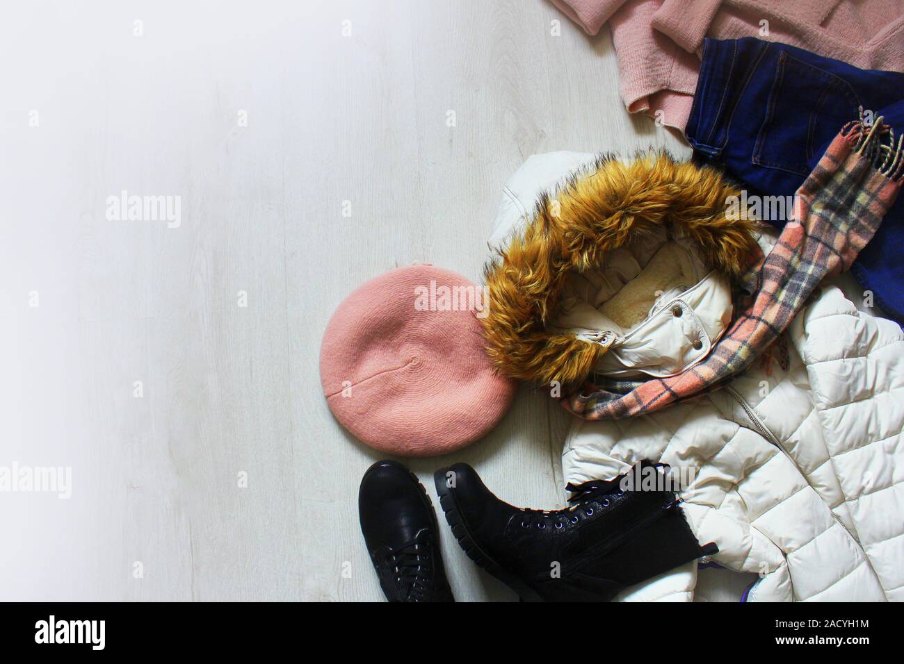 Un ensemble d'hiver à la mode des vêtements de femmes. Chandail de laine, chaussures, jeans, manteau, chapeau et un foulard blanc sur fond de bois. Banque D'Images