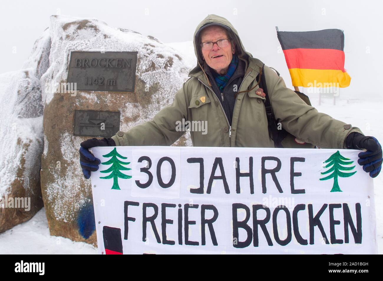 Wernigerode, Allemagne. 06Th Dec, 2019. Le randonneur record Benno Schmidt, connu sous le nom de Benno Brocken, se dresse avec une bannière sur le plateau du Brocken. La banderole dit '30 ans de Brocken.' Benno Schmidt a 30 ans, le 03 décembre 1989, parmi les randonneurs qui ont exigé l'ouverture de la porte à l'entrée de la zone militaire. Depuis, il avait marché le Brocken 8870 fois. Credit : Klaus-Dietmar Gabbert/dpa-Zentralbild/dpa/Alamy Live News Banque D'Images