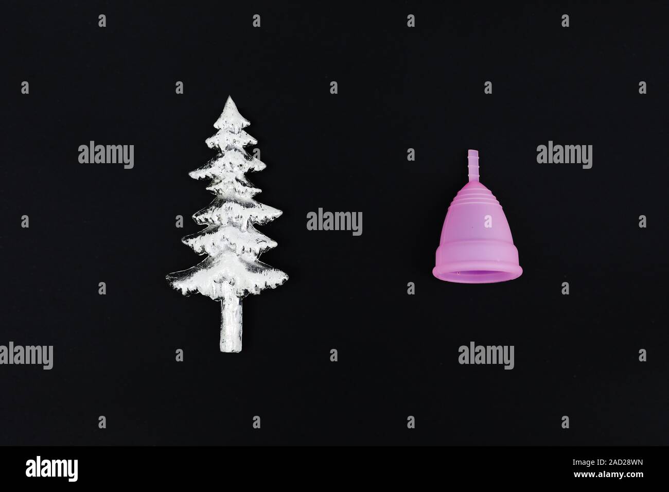 Coupe menstruelle rose sur fond noir en céramique et arbre de Noël. Produit d'hygiène féminine, télévision lay, copiez l'espace. L'horizontale. Banque D'Images